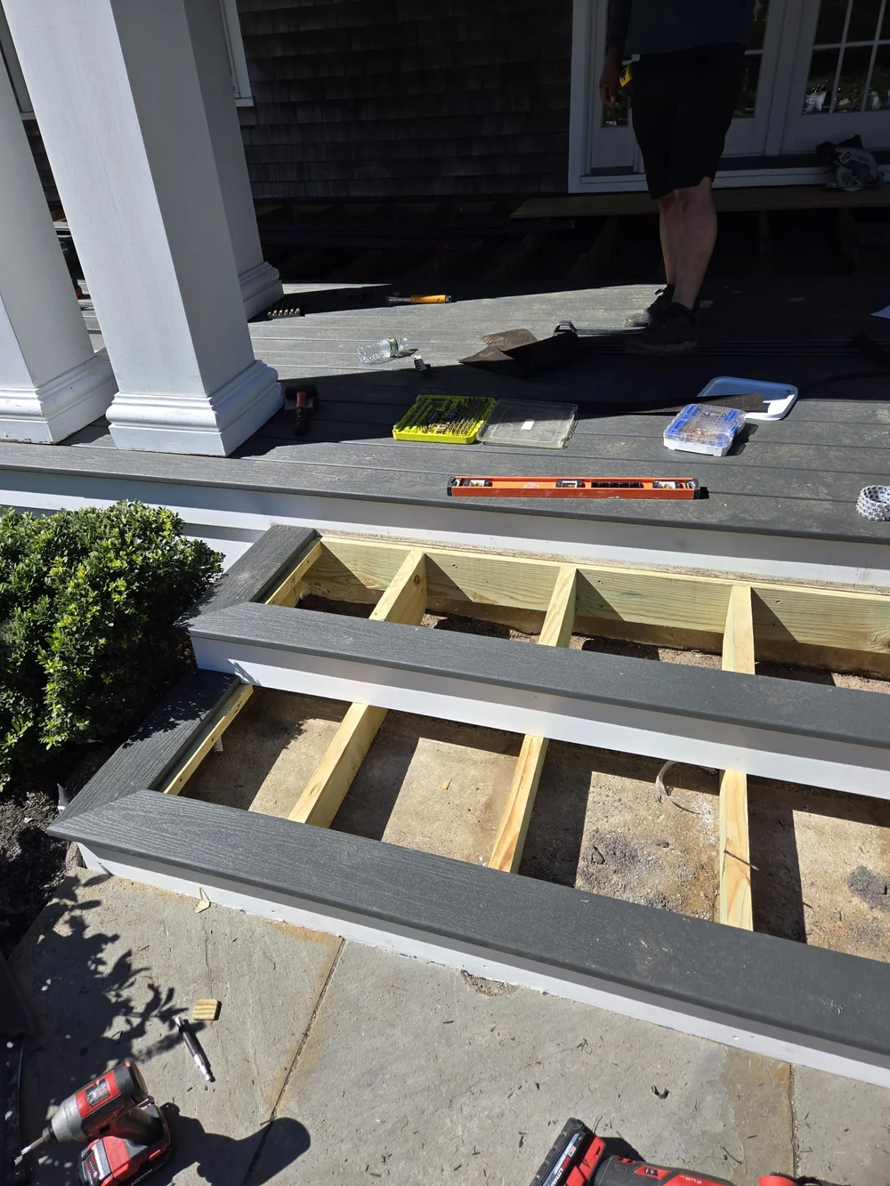 Downstairs porch and steps during installation, with gray decking, white risers, exposed step framing and tools