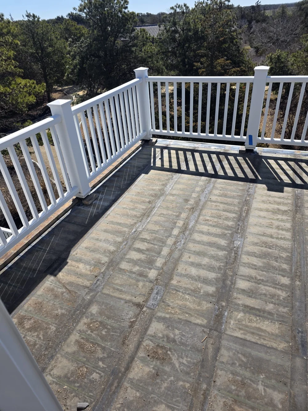 Corner of the upstairs deck during preparation, with exposed surface, white railings and blue tape at post bases