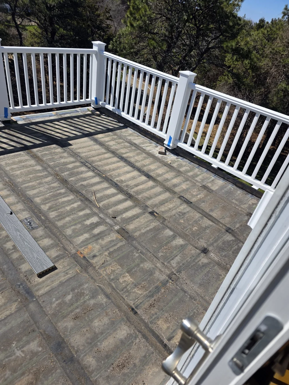 Upstairs deck during preparation, with the old surface exposed beneath white railings and a loose gray deck board