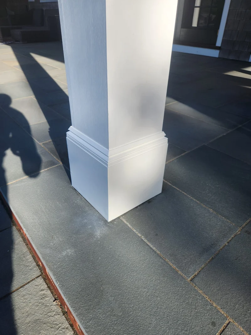 Close-up of a white exterior column and its layered base trim on a stone terrace