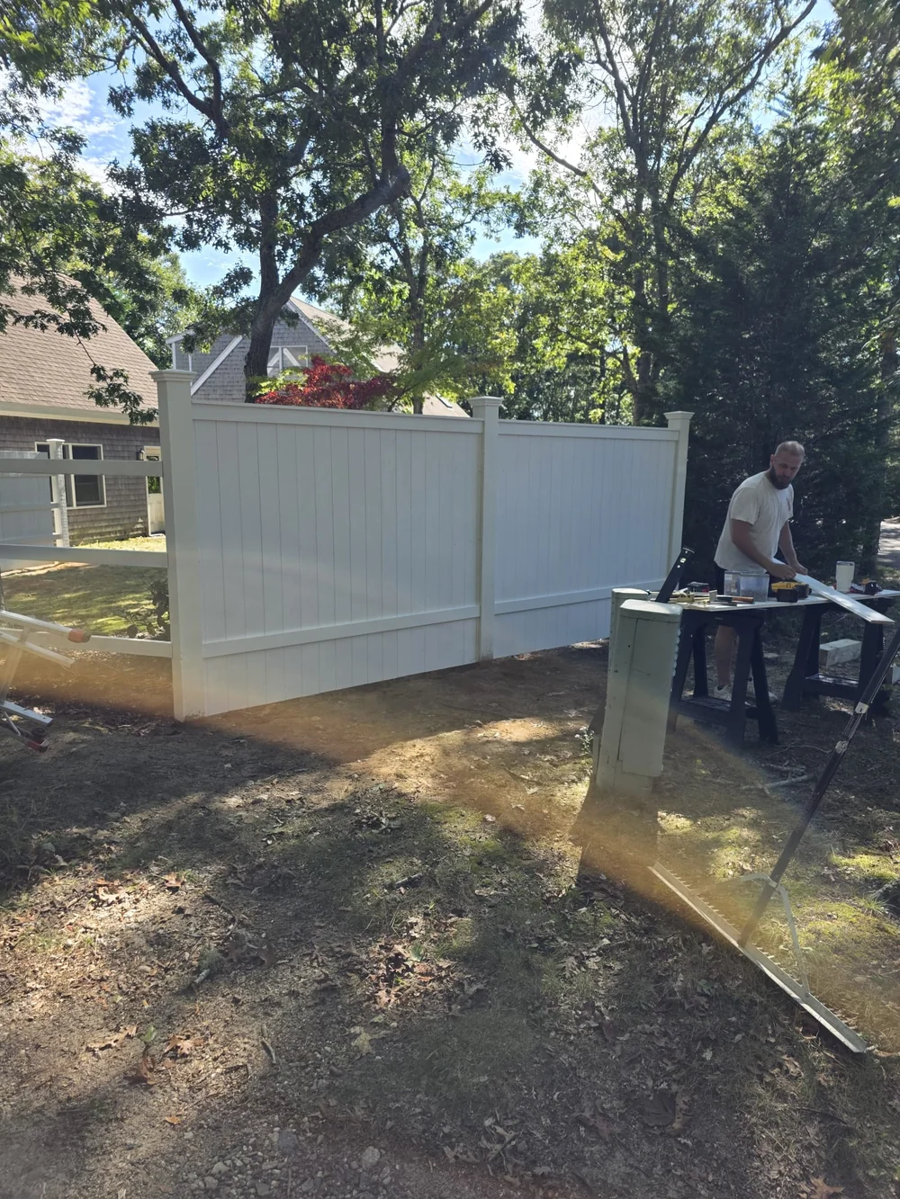 White privacy fence panels and capped posts during installation, with a worker and tools alongside