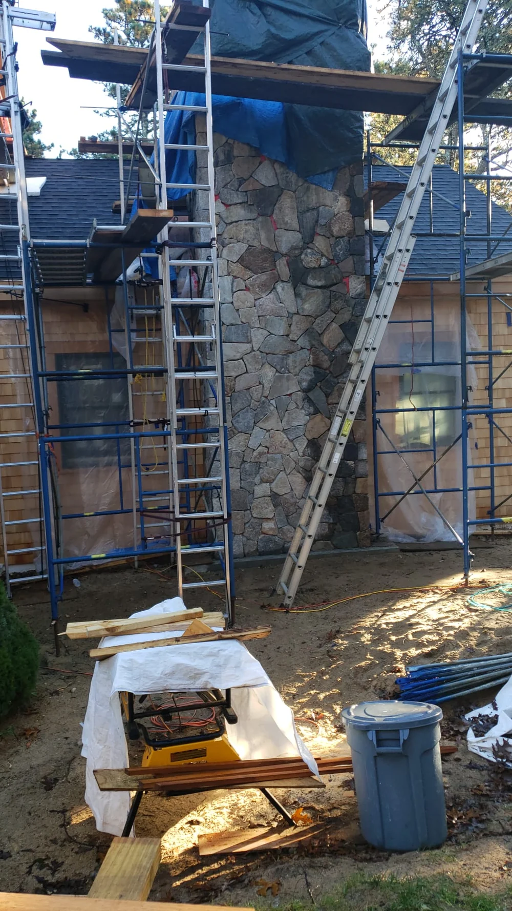 Exterior stone chimney surrounded by scaffolding and ladders during fireplace installation