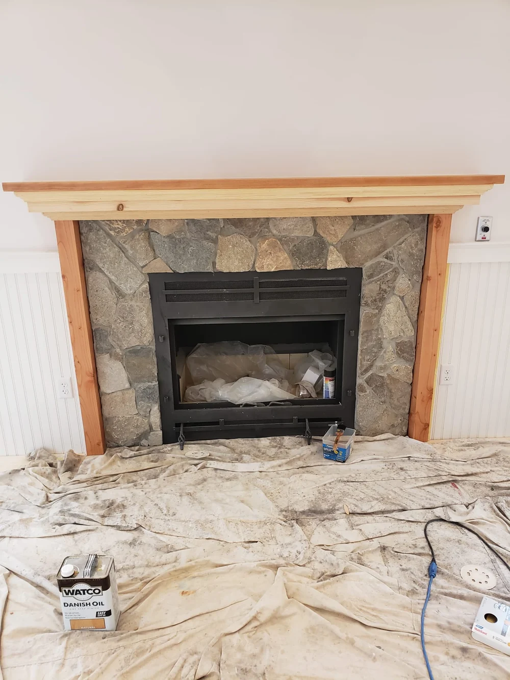 New interior fireplace with a stone surround and wood mantel, with drop cloths and tools still in place