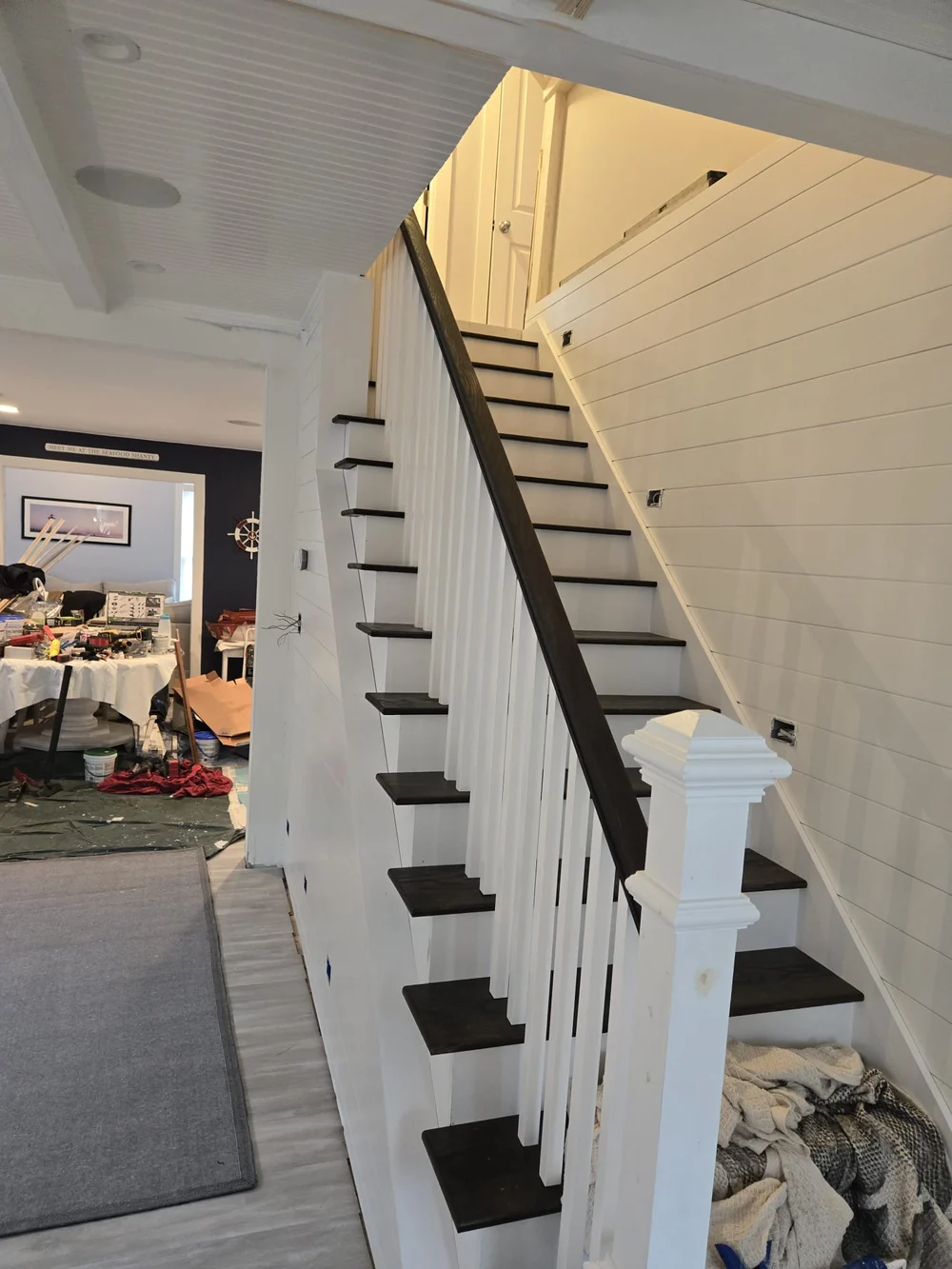 After renovation: staircase with dark wood treads and handrail, white balusters and paneled walls, with finishing materials still present