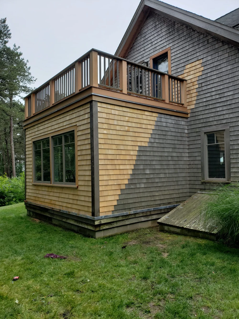 Corner view of a shingled home showing fresh shingles beside existing siding and wood balcony railings above