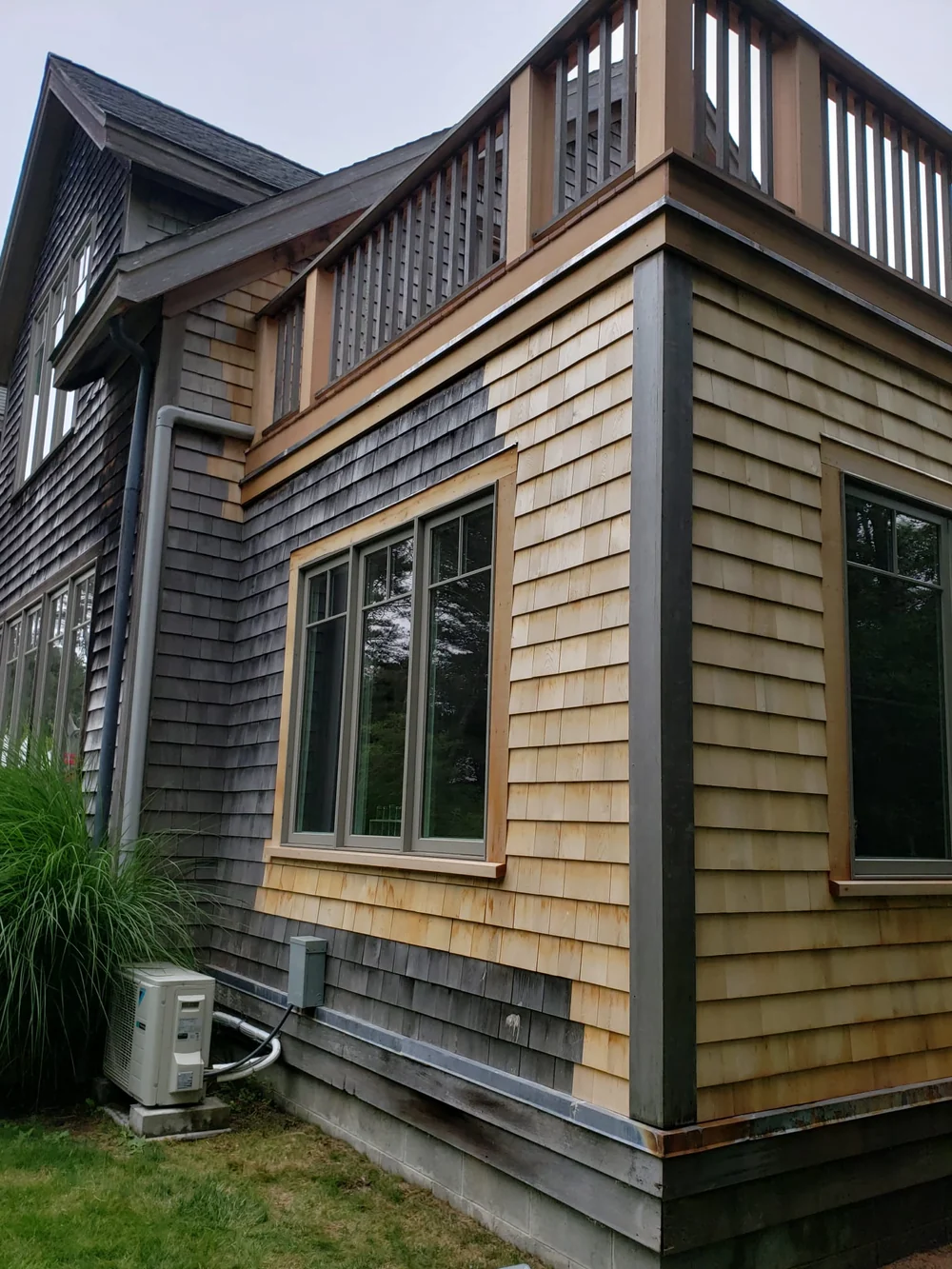 Fresh wood shingles and window trim beside weathered gray siding, below an upper balcony